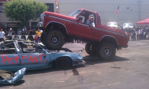 1978 Ford Bronco - A red pickup truck is positioned on top of a heavily damaged blue car, suggesting a demolition derby or similar event.