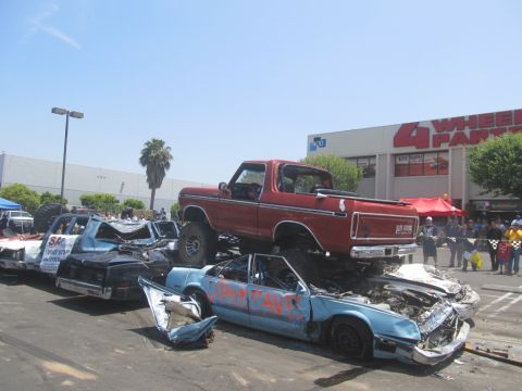 1978 Ford Bronco - A red pickup truck is piled on top of several wrecked cars in a junkyard setting.