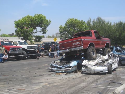 1978 Ford Bronco - A red 1978 Ford Bronco is perched atop a pile of wrecked vehicles at an outdoor event.