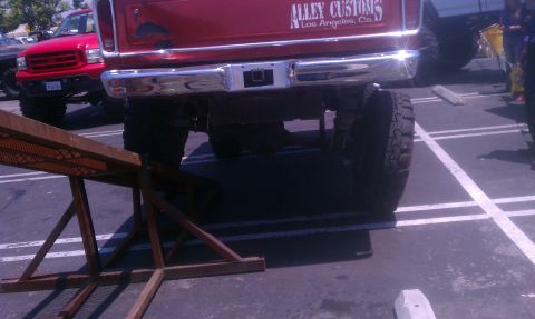1978 Ford Bronco - A red pickup truck with custom text on the tailgate is parked in a lot with another vehicle visible.