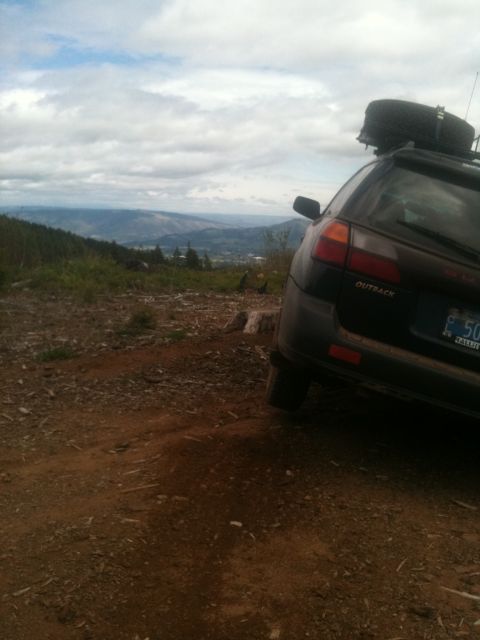 2005 Jeep Wrangler - A dark Subaru Outback is parked on a dirt road, its rear facing the camera, with a spare tire mounted on the roof rack and a scenic valley…