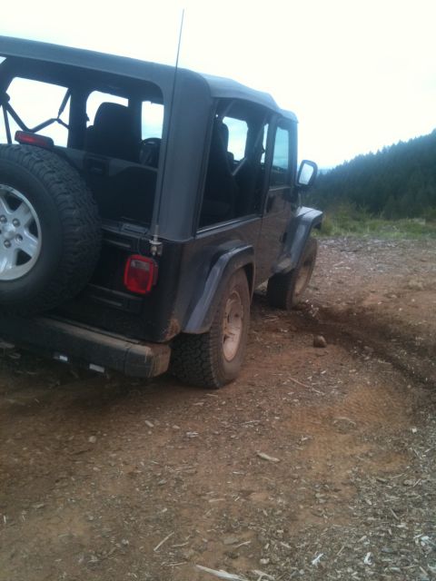 2005 Jeep Wrangler - A black Jeep Wrangler is parked on a dirt road, with a wooded hillside visible in the distance.