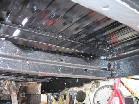 1979 Ford Bronco - The undercarriage of a vehicle is shown, with a focus on the frame and structural components, and a bicycle wheel in the background.