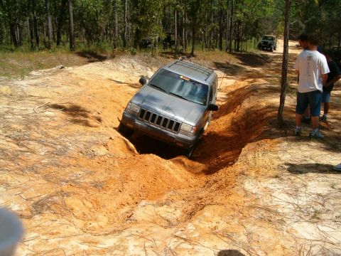 1991 Ford Bronco - A silver Jeep Grand Cherokee navigates a challenging rutted dirt path, with another Jeep visible in the distance.