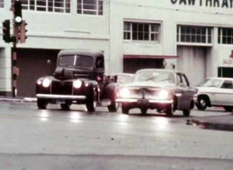 1969 Lincoln Continental - A dark truck and a light sedan are seen from the front on a wet street.