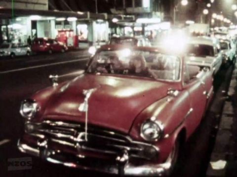 1969 Lincoln Continental - A red convertible cruises down a city street at night, with other vehicles visible.