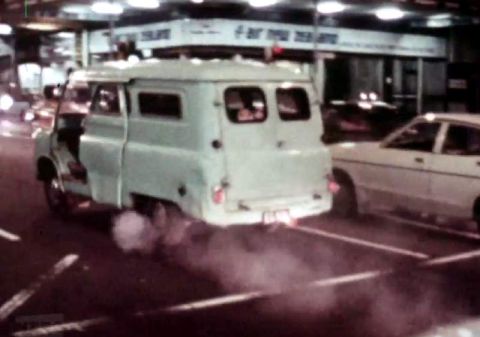 1969 Lincoln Continental - A light blue van is seen from the rear, emitting smoke as it drives on a street.