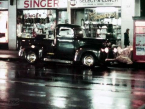 1969 Lincoln Continental - A dark-colored pickup truck is parked on a wet street at night, with storefronts in the background.