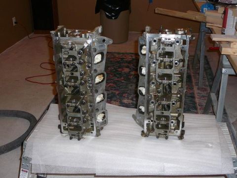 1997 Mercury Grand Marquis - Two engine cylinder heads are displayed on a white protective surface in a room with a carpet and trash can.