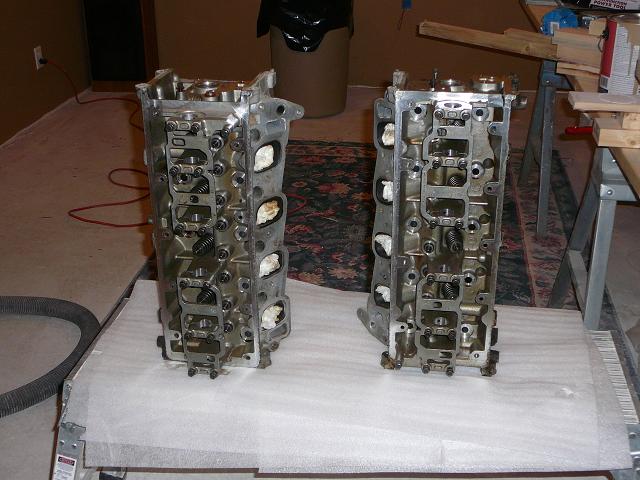 two engine cylinder heads on a white surface, one on the left, one on the right