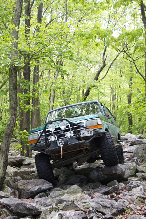 1996 Ford Bronco - Green 1996 Ford Bronco navigating a rocky off-road course in a forest.