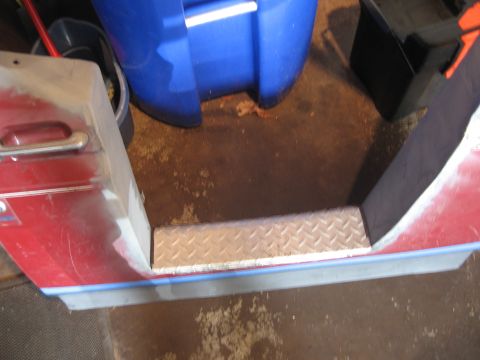 1996 Ford Bronco - Overhead close-up of the bottom of a dark red truck door under repair in a garage, with a bare aluminum diamond-plate step panel fitted int…