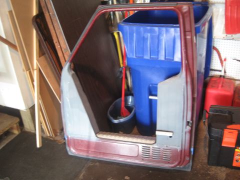 1996 Ford Bronco - Two-tone maroon and silver truck door shell stripped of trim, leaning in a garage beside blue and red trash bins.