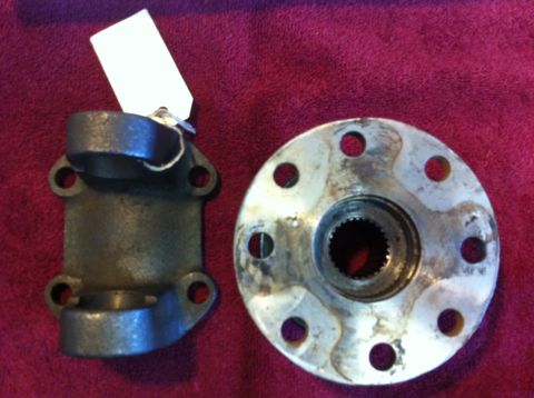 1987 Suzuki Samurai - Two automotive drivetrain components, a U-joint yoke and a flange, are displayed on a red surface.