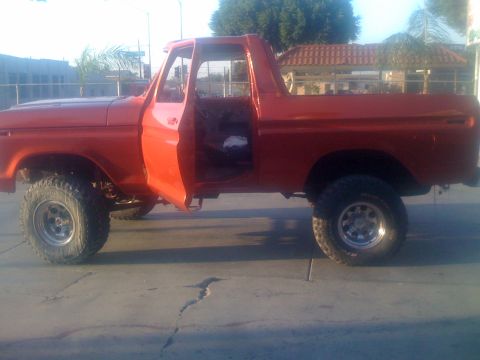 1978 Ford Bronco - Side view of an orange 1978 Ford Bronco with its doors open, showing its interior and lifted suspension.