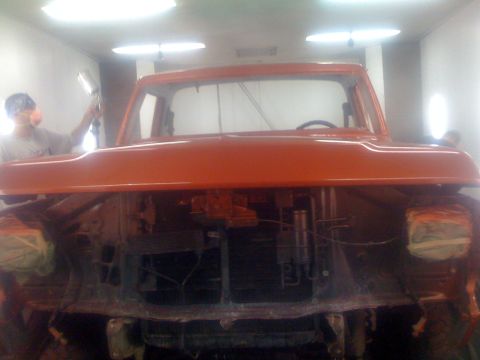 1978 Ford Bronco - A person sprays paint on an orange truck in a booth, with the front end partially disassembled.