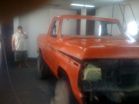 1978 Ford Bronco - A person stands near an orange pickup truck undergoing work in a garage.