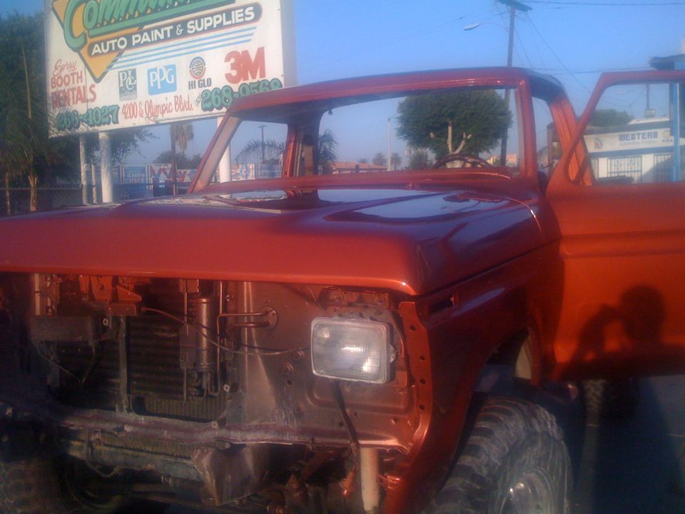 Orange pickup truck with doors open, front end disassembled, parked outside auto paint shop