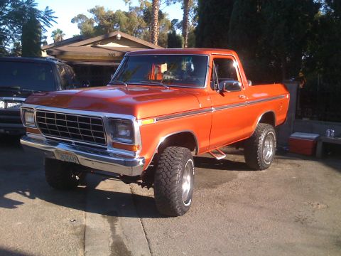 1978 Ford Bronco - This orange pickup truck is parked in a driveway with a house and trees in the background.