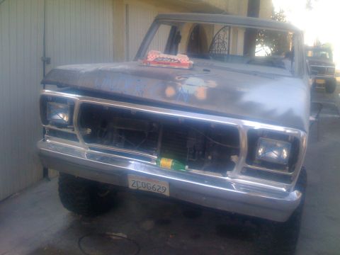 1978 Ford Bronco - A primer-gray pickup truck sits in front of a garage door, with another vehicle partially visible in the background.