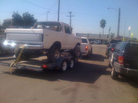 1978 Ford Bronco - A white SUV is being transported on a trailer, with other vehicles visible on the road.