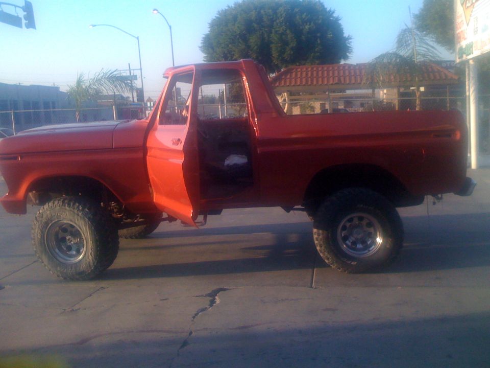 Red pickup truck with doors open, lifted suspension, and off-road tires