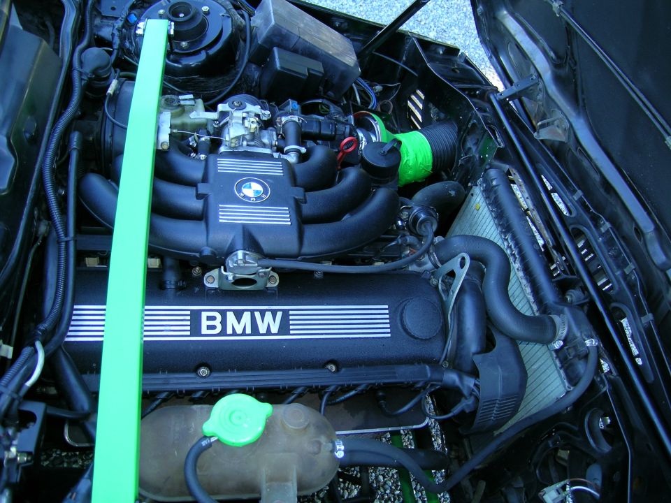 BMW engine bay with a green strut bar, black intake manifold, and "BMW" lettering on the valve cover