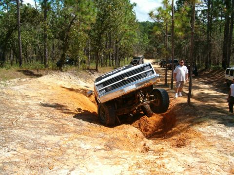 1991 Ford Bronco - A lifted Chevrolet pickup truck navigates a challenging off-road terrain with other vehicles present.