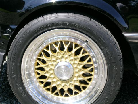 1982 BMW 3 Series - Close-up of a gold mesh wheel and tire on a black vehicle.