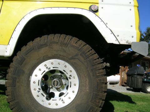 1966 Ford Bronco - Close-up of a yellow and white SUV's fender and wheel, a large off-road tire and custom rim with 'TR' markings.