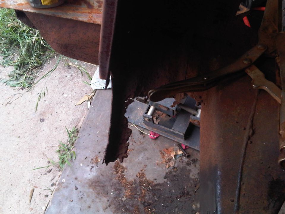 rusted metal panel held by clamp, showing significant rust and damage