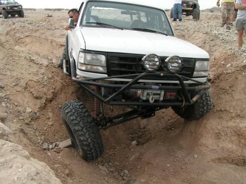 1988 Ford Bronco - A white Ford Bronco navigates a challenging off-road terrain, with another vehicle visible in the background.