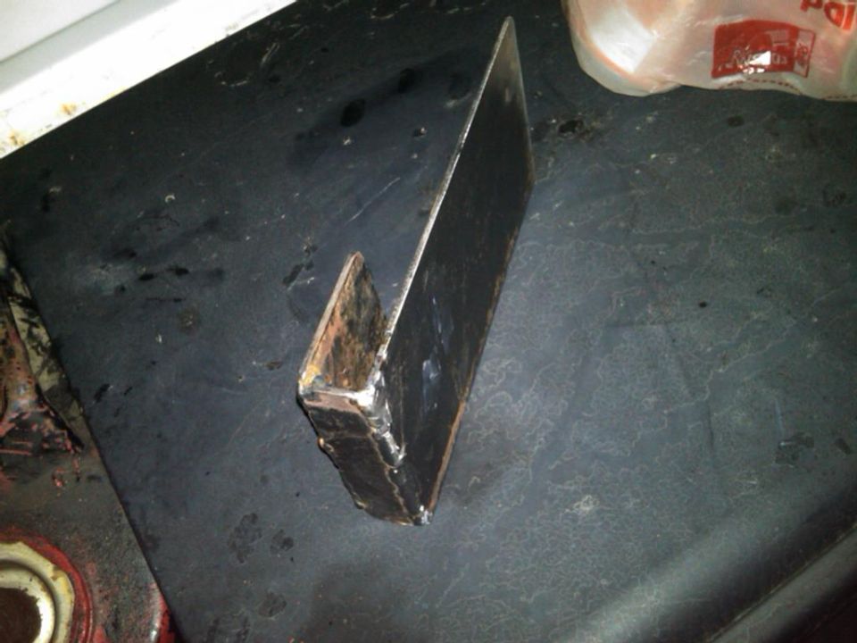Welded metal bracket with a hook shape, resting on a dark surface