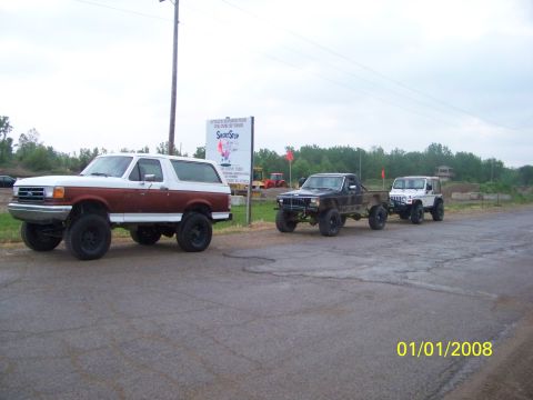 1989 Ford Bronco - A lifted 1989 Ford Bronco is parked on the side of the road, with a black pickup truck and a white Jeep following behind.