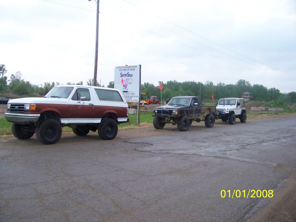 White and brown lifted 1989 Ford Bronco parked on asphalt, with other vehicles behind it
