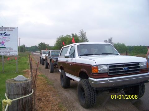 1989 Ford Bronco - Several off-road vehicles, including a 1989 Ford Bronco, are lined up on a dirt road.