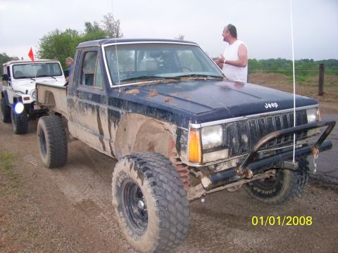 1989 Ford Bronco - Two off-road vehicles, a Jeep Comanche and a Jeep Wrangler, are covered in mud on a dirt road.