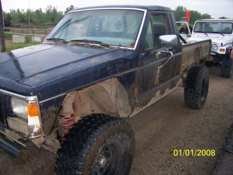 1989 Ford Bronco - A muddy dark blue pickup truck is parked next to a white Jeep on a dirt road.