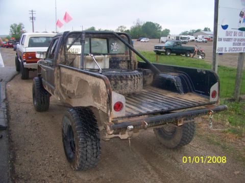 1989 Ford Bronco - A heavily modified and mud-splattered pickup truck is seen from the rear, parked next to another vehicle.