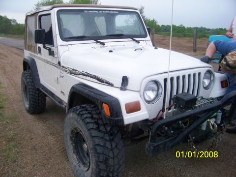 1989 Ford Bronco - A white Jeep Wrangler is parked on a dirt road with a person working on its front bumper.