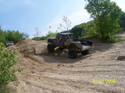 1989 Ford Bronco - Two off-road vehicles navigate a sandy terrain under a clear blue sky.