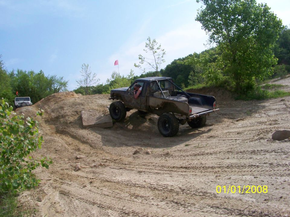Muddy pickup truck with roll cage driving on a dirt hill, another white SUV in background