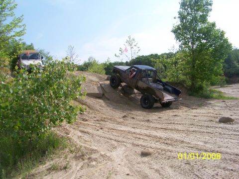 1989 Ford Bronco - Two off-road vehicles navigate a sandy terrain with trees in the background.