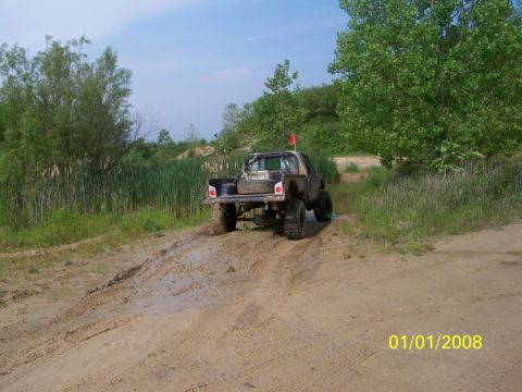 1989 Ford Bronco - A modified pickup truck navigates a muddy off-road trail under a clear sky.