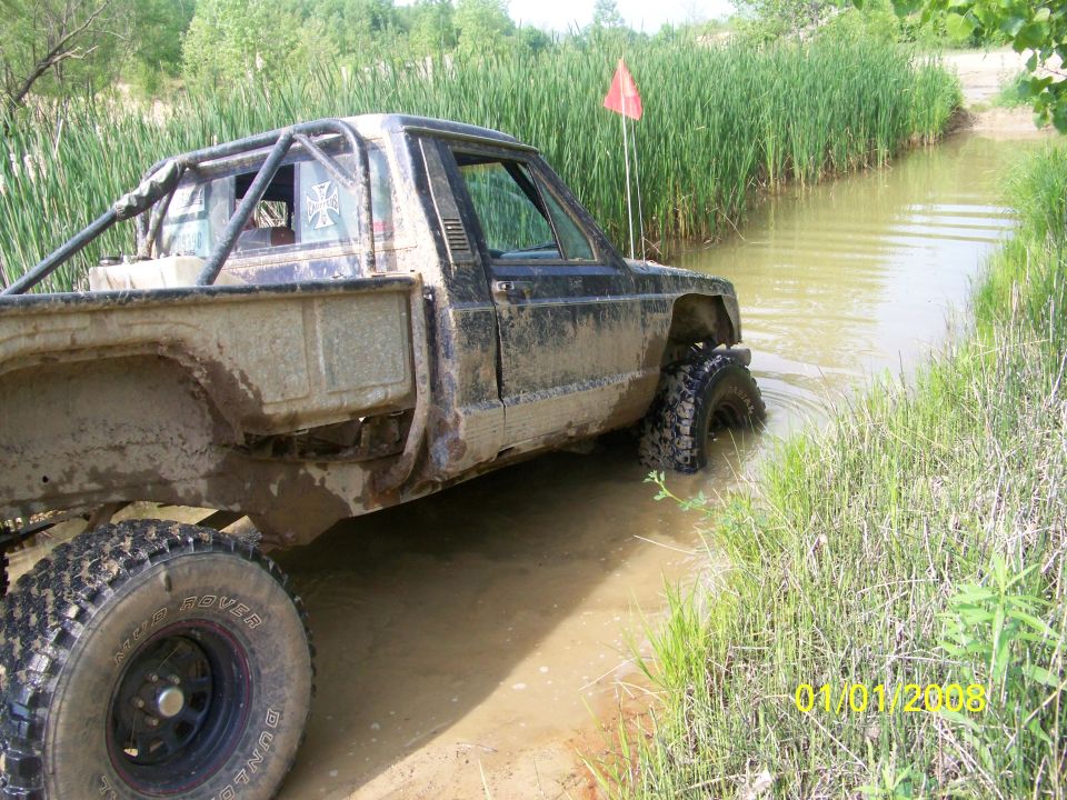 Mud-covered pickup truck with roll cage driving through water, side view