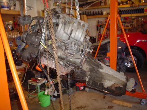 1990 Ford Bronco - Engine and transmission assembly hoisted for removal or installation in a garage setting.