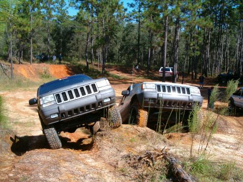 1991 Ford Bronco - Two Jeep Grand Cherokees tackle a challenging off-road course in a wooded area.