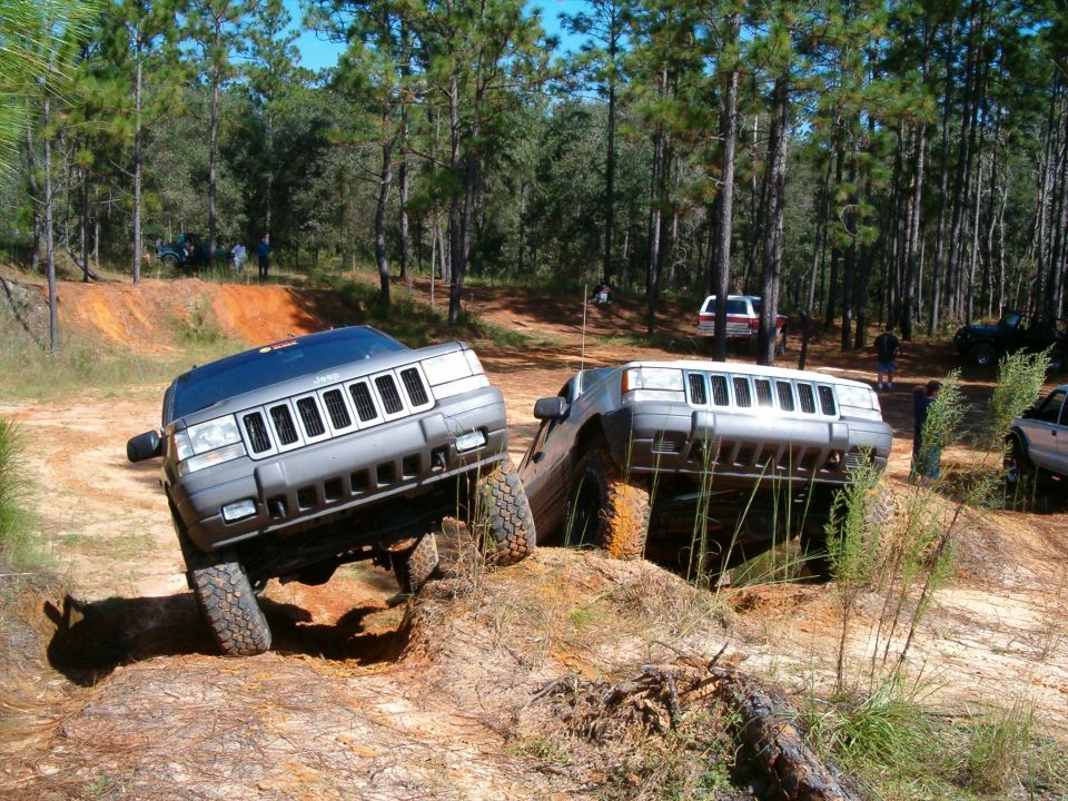 Two lifted gray and silver Jeep Grand Cherokees climbing a sand pit at an off-road park
