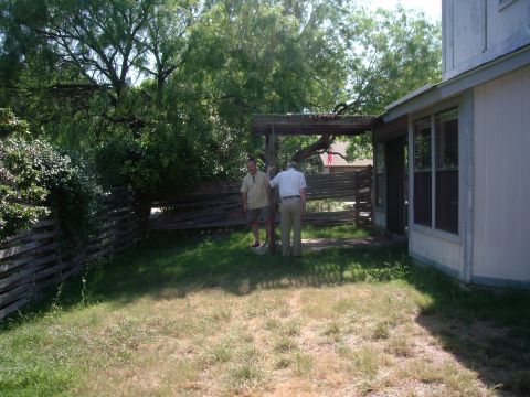 1983 Ford 427 - Two men stand in a backyard with a wooden fence and a covered patio area.