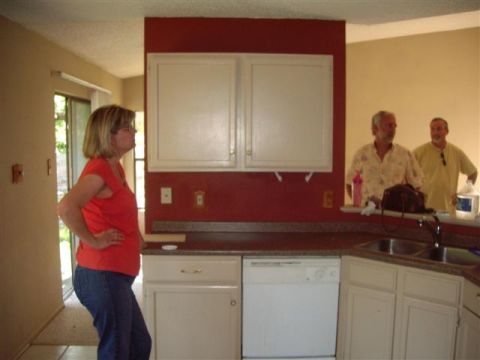 1983 Ford 427 - A woman stands in a kitchen while two men are visible in the background.
